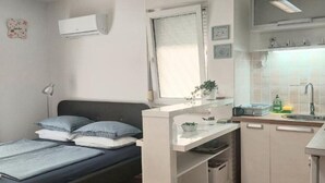Une pièce de taille modeste comprenant un lit, une petite kitchenette, une fenêtre et un appareil de climatisation.