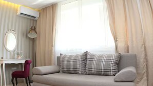 Ein modernes Zimmer mit einer Couch, einem Schreibtisch, einem Stuhl und einem großen Fenster mit Vorhängen.