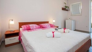 Ein Schlafzimmer mit Bett, Nachttischen, einer Lampe, einer kleinen Pflanze, einem Heizkörper und einem Fenster.