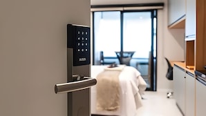 Quarto de hotel moderno com fechadura digital, cama, área de refeições e vista para o exterior.