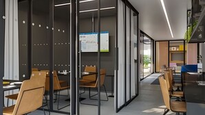 Um espaço de escritório moderno com divisórias de vidro, cadeiras de madeira e um quadro branco à vista.
