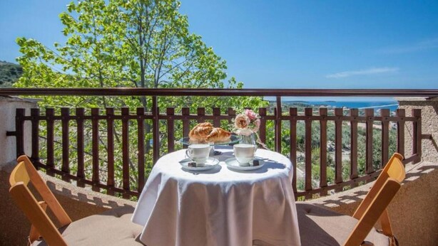 A balcony with a table set for two, overlooking a scenic view with a tree and a body of water. - Guest House Stay & Smile Dolac Primošten - Studio with Sea View and Balcony (Primosten)