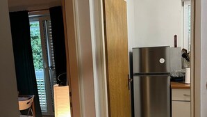 Cozinha com geladeira de aço inoxidável, porta de madeira e vista para o exterior.