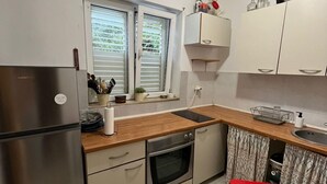 Cozinha compacta com geladeira, forno, pia e janela com persianas.