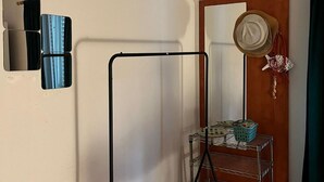 Quarto com uma estante de metal, um espelho, uma porta com chapéu e chaves, e uma pequena mesa com uma cesta.