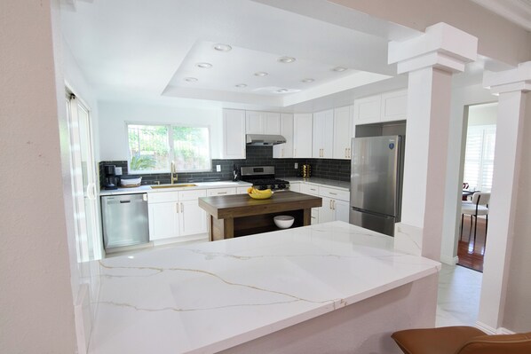 Una cocina moderna con armarios blancos, encimera de mármol y electrodomésticos de acero inoxidable.