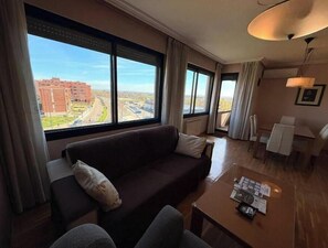 Ein Hotelzimmer mit großem Fenster, einer Couch, einem Esstisch und einer Lampe.