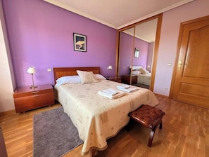 A bedroom with a bed, bedside tables, a bench, a mirror, and a door.