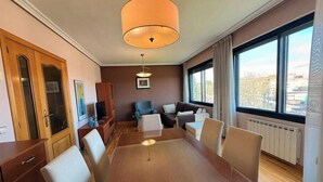 Hotellihuone, jossa on puinen ruokapöytä, kaksi sohvaa, televisio ja suuri ikkuna.