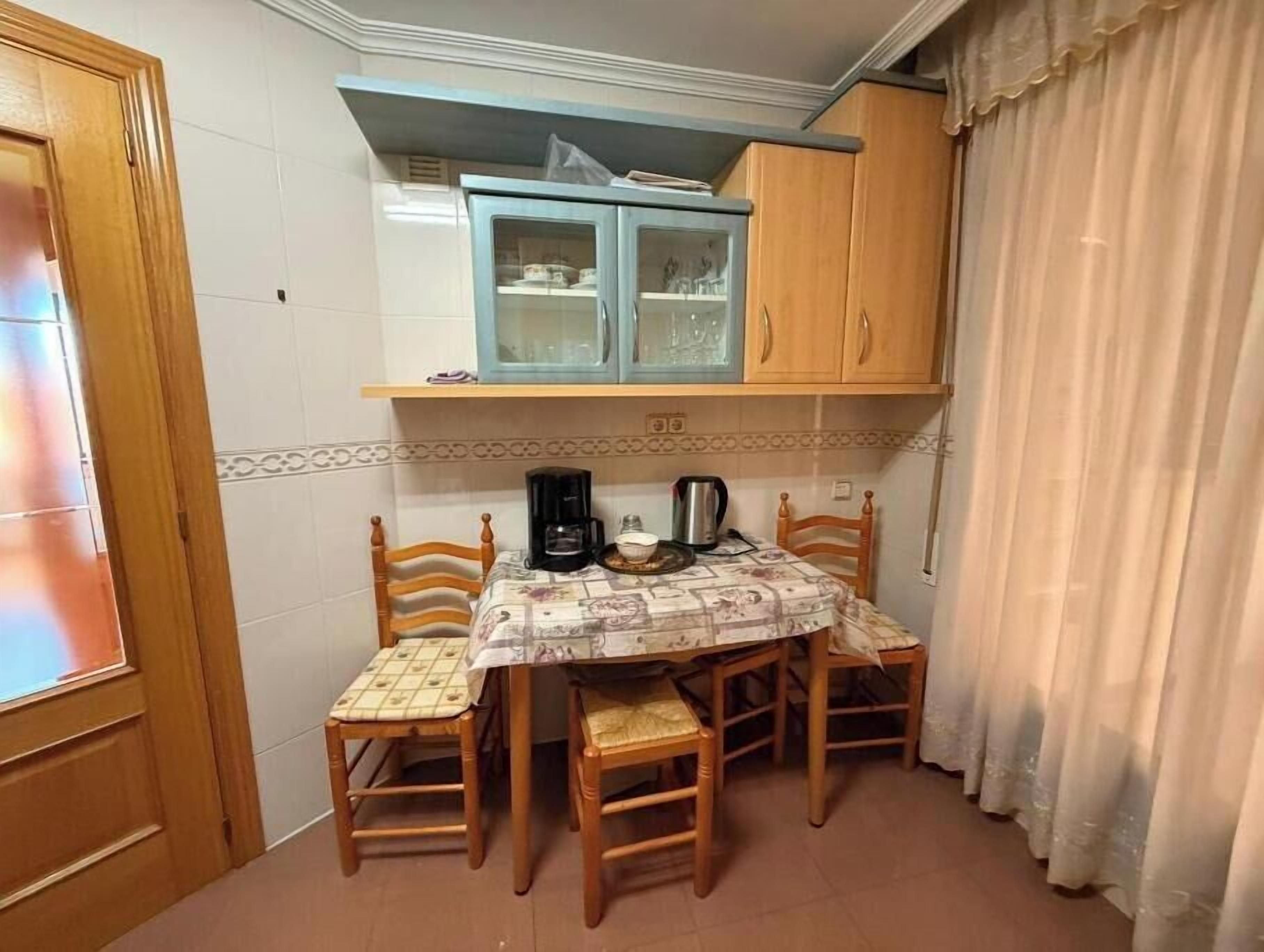 A compact kitchen with a table, chairs, a coffee maker, and cabinets.