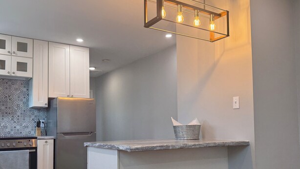 A modern kitchen with white cabinets, a stainless steel refrigerator, a built-in oven, and a bar area with stools. - No Cleaning Fee  Quiet Stay Near Base & Memphis  Fast WiFi (Millington)