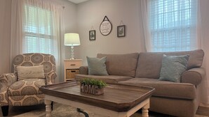 A living room with a patterned armchair, a brown sofa, a wooden coffee table with 'HOME' and a plant, and a lamp. - No Cleaning Fee  Quiet Stay Near Base & Memphis  Fast WiFi (Millington)