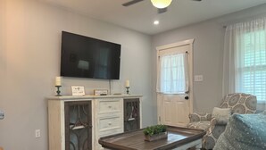 A living room with a flat-screen TV, a coffee table with a plant, a sofa with patterned cushions, and a door with a window. - No Cleaning Fee  Quiet Stay Near Base & Memphis  Fast WiFi (Millington)