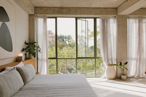 Ein Schlafzimmer mit einem großen Bett, Blick durch raumhohe Fenster und einer Zimmerpflanze am Fenster.