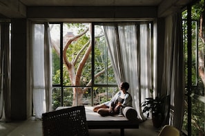 Ein Zimmer mit großem Fenster, einem Bett, einem Sessel und einem Blumentopf.