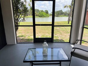 A room with a glass table, a chair, and a view of a lake through a large window. - Serene 2-bedroom house with water view in charming Venice (Venice)
