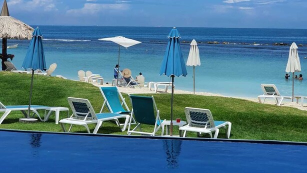 Vista de la piscina con sillas de descanso, sombrillas y el mar al fondo.