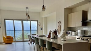 Cocina moderna con una isla central, taburetes de bar y vista al mar a través de amplios ventanales correderos.