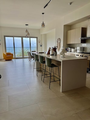 A modern kitchen with a central island, bar stools, and a view of the sea through large sliding doors. - Ocean View Apartment : Playa Escondida, Panama (María Chiquita)