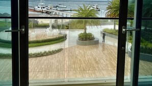 Vista desde un balcón sobre un puerto deportivo con barcos, una palmera y una zona pavimentada con asientos.