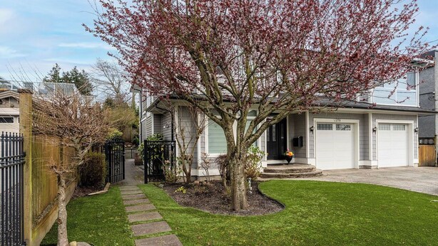 A residential property with a well-maintained lawn, a stone pathway, a garage, and a tree with pink blossoms.