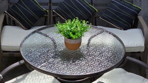 A round glass table with a potted plant, surrounded by four chairs with cushions.