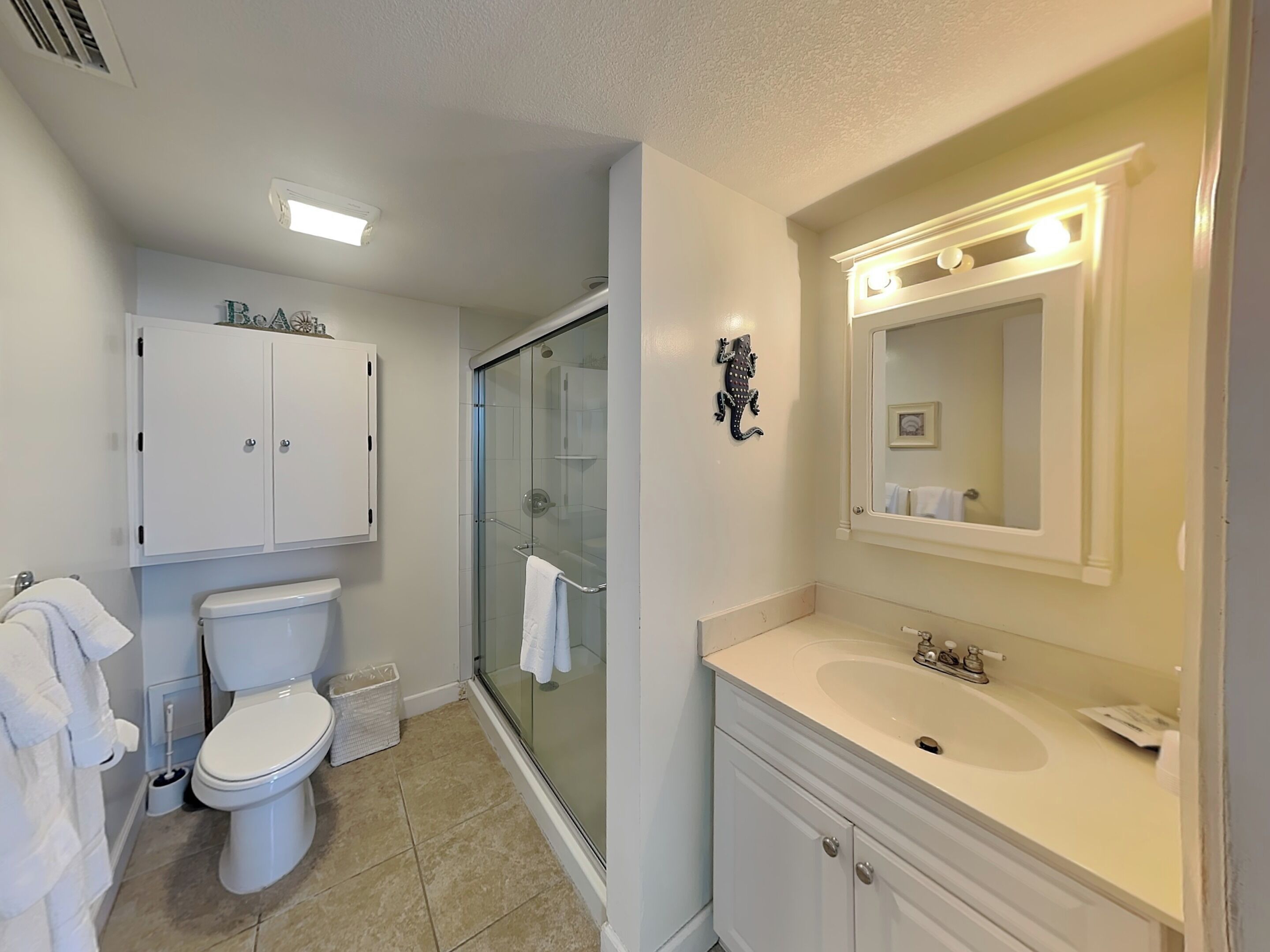 A bathroom with a toilet, a glass-enclosed shower, a sink with a mirror, and a cabinet above the toilet.