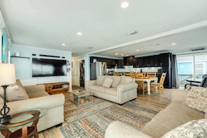 A modern living room with a large TV, a sofa, a coffee table, and a dining area with a table and chairs.
