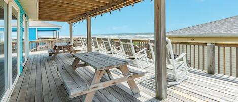 Une terrasse en bois avec des tables et des chaises pour pique-niquer, offrant une vue sur l’océan.