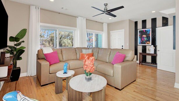 A modern living room with a beige sectional sofa, two round coffee tables, a ceiling fan, and large windows. - House of Whimsy (Tybee Island)