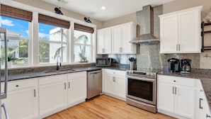 A modern kitchen with white cabinets, a stainless steel oven, a microwave, and a coffee maker. - House of Whimsy (Tybee Island)