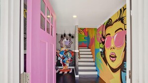 A hallway with a pink door, a staircase, and a mural on the wall. - House of Whimsy (Tybee Island)