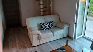 A living room with a sofa, a patterned pillow, a wooden coffee table, a staircase, and a sliding glass door. - B & B Sotto il lago (Nemoli)
