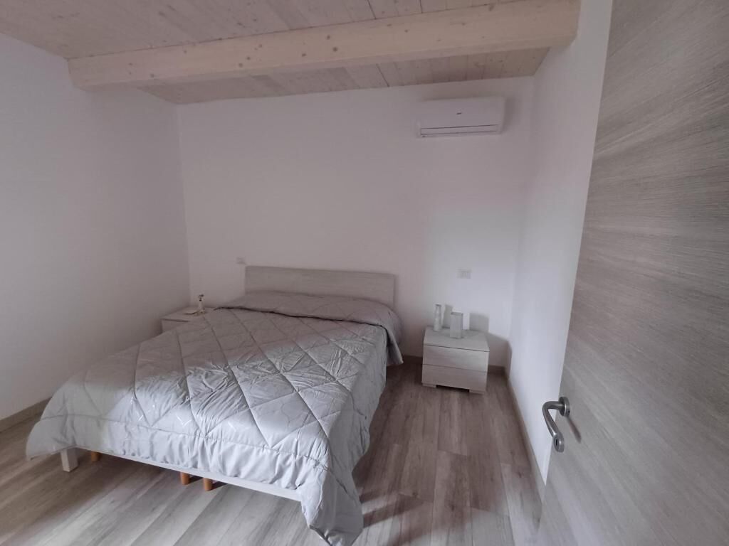 Een slaapkamer met een bed, nachtkastje, airconditioning en een houten vloer.