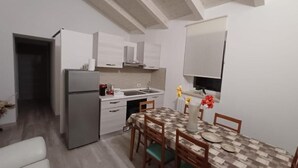 A compact kitchen with modern appliances, a dining table with chairs, and a flat-screen TV mounted on the wall. - B & B Sotto il lago (Nemoli)