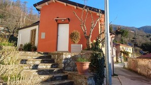 A building with a red facade, a white door, and a small garden with a tree and a potted plant. - B & B Sotto il lago (Nemoli)