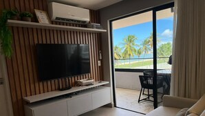 A modern living room with a flat-screen TV, a sofa, a balcony with a view of palm trees and the ocean. - Altamare 203 - Luxury and comfort right on the sand at Caribessa beach. (João Pessoa)