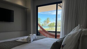 A hotel room with a bed, a TV, a hammock, and a view of palm trees and a beach. - Altamare 203 - Luxury and comfort right on the sand at Caribessa beach. (João Pessoa)