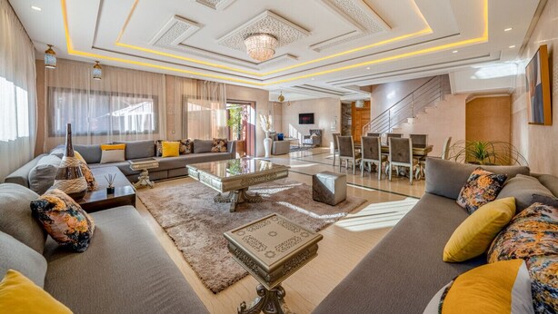 Een ruime woonkamer met een zithoek, een salontafel en een eethoek met stoelen en een trap.