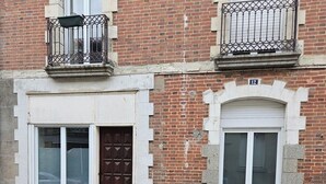 A building with a brick facade, two windows with white frames, a brown door, and a small balcony with a metal railing.