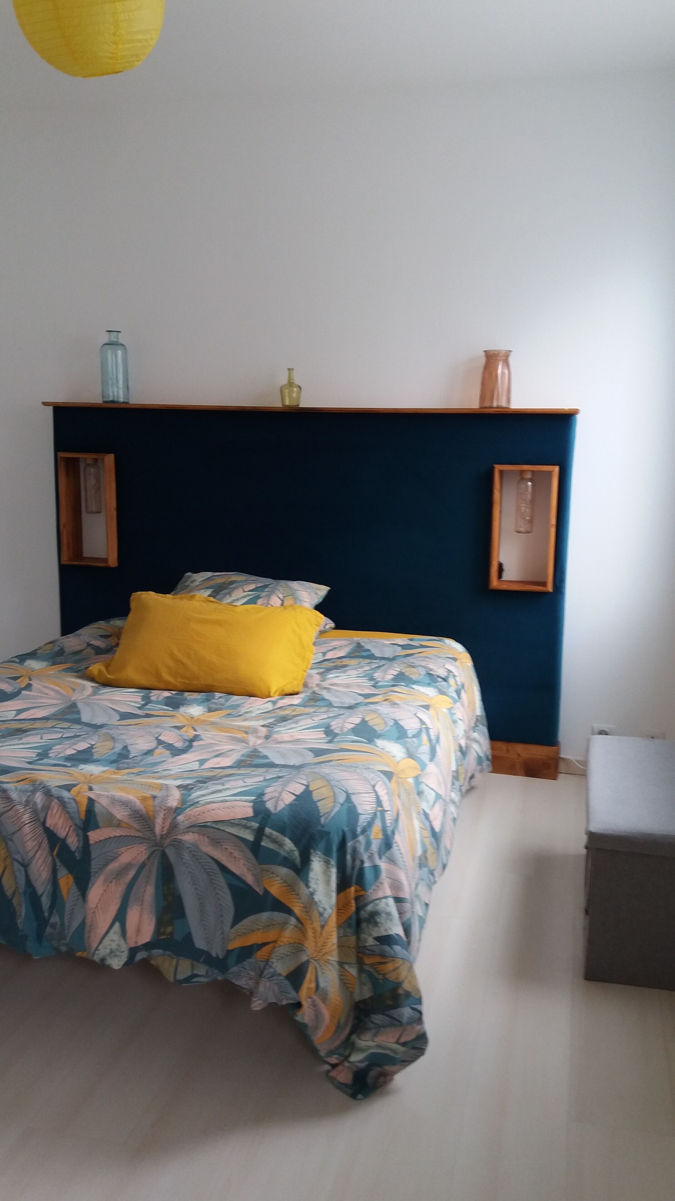 Ein Schlafzimmer mit einem Bett, einem Nachttisch, einer Kommode und einem an der Wand montierten Regal mit Dekoration.