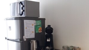 A kitchenette with a refrigerator, coffee maker, and jars on the counter.
