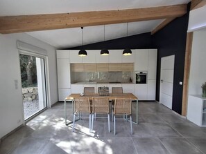 A modern kitchen with white cabinetry, a dining table with chairs, pendant lights, and a large window. - Bioclimatic villa for 8, swimming pool, quiet location (Grasse)