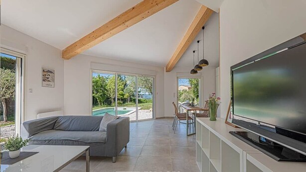Un salon moderne doté d’un grand téléviseur, d’un canapé, d’un coin repas et offrant une vue sur une piscine.