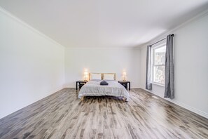 A bedroom with a bed, two bedside tables, a window with curtains, and a wooden floor.