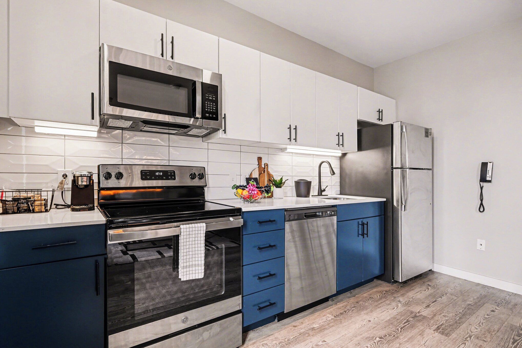 A modern kitchen with stainless steel appliances, white cabinets, and blue drawers.