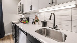 A modern kitchen with white cabinets, a stainless steel sink, and a microwave. - Music Row Hotel (Nashville)