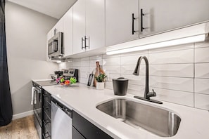A modern kitchen with white cabinets, a stainless steel sink, and a microwave. - Motif (Nashville)