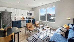 A modern kitchen with white cabinets, a microwave, and a refrigerator. There is a dining area with a table and chairs, and a living area with a sofa and a coffee table. - Music Row Hotel (Nashville)