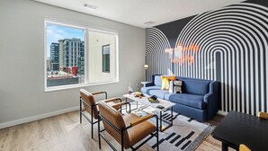 A modern living room with a large window, a blue sofa, a coffee table, and a patterned wall. - Music Row Hotel (Nashville)